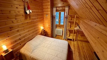 A cozy wooden cabin bedroom with a bed, a nightstand, a shelf, and a window with curtains.