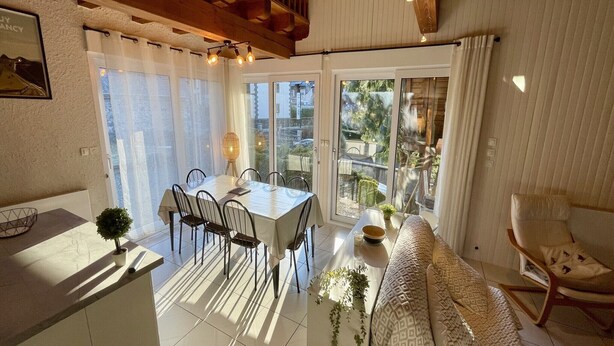 Eine moderne Küche mit Essbereich, einer Couch und einem Sessel. Ein Fenster mit Vorhängen bietet Blick ins Freie.
