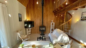 Ein gemütliches Wohnzimmer mit Kamin, Holzwänden, einem Fernseher und einer Treppe.