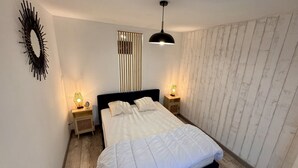 Ein Schlafzimmer mit einem Bett, zwei Nachttischen mit Lampen, einer modernen Pendelleuchte, einer Wanddekoration und einem Holzboden.