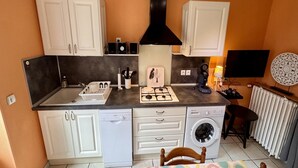 Een kleine keuken met witte kastjes, een gasfornuis, een wasmachine en een televisie.