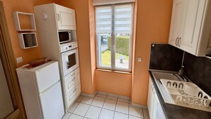 Een functionele keuken met witte kastjes, een koelkast, een magnetron en een spoelbak.