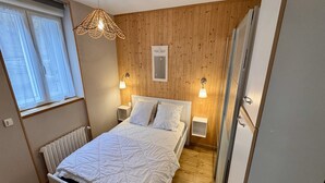 Een slaapkamer met een bed, nachtlampjes, een radiator, houten wanden en een raam met gordijnen.