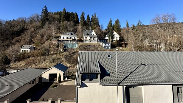 Ein Wohngebiet mit Häusern an einem Hang, einem klaren Himmel und einem gebäudeartigen Bauwerk mit Metallbedachung im Vordergrund.