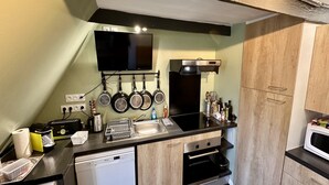 Eine kompakte Küche mit schwarzer Arbeitsplatte, Edelstahlgeräten, einem an der Wand montierten Fernseher und Holzschränken.