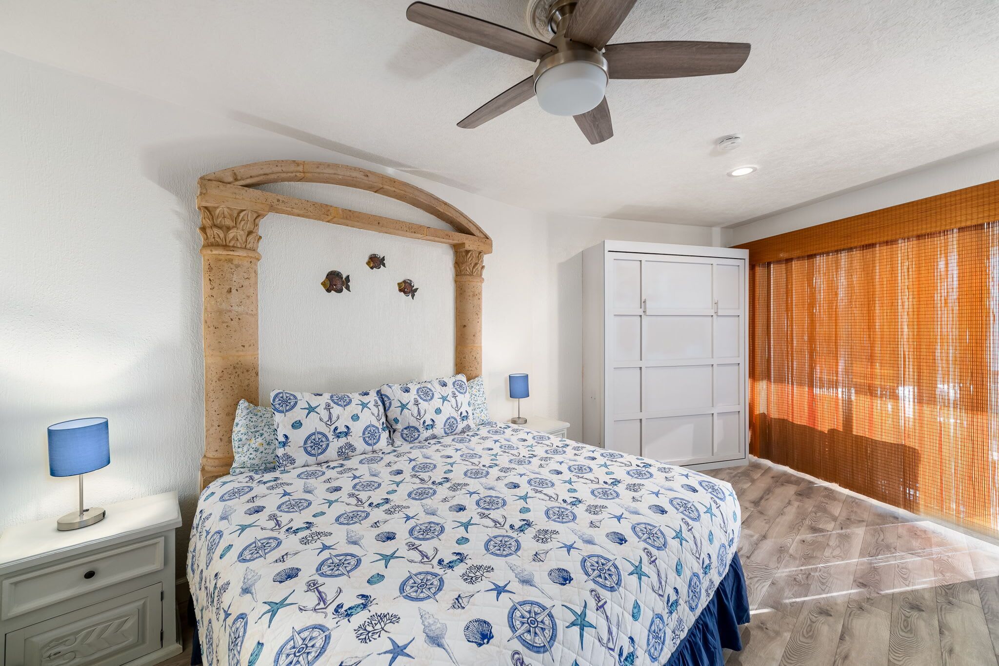 A bedroom with a bed, a ceiling fan, a wardrobe, and a window with curtains.