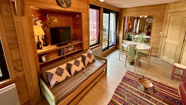 Ein gemütliches Holzhaus-Interieur mit einer Couch, einem Fernseher, einem Esstisch und Stühlen.