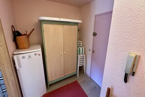 Une pièce de taille modeste, avec une armoire en bois, un petit réfrigérateur, un tapis rouge et un téléphone blanc fixé au mur.