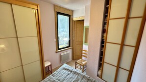 Ein kleines Schlafzimmer mit einem Bett, einem Sessel, einem Fenster und einem Kleiderschrank.