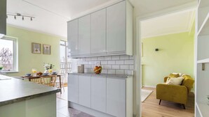 A modern kitchen with white cabinets, a marble countertop, and a dining area with a table and chairs. - Cozy 1BR Near Hyde Park & Notting Hill (London)