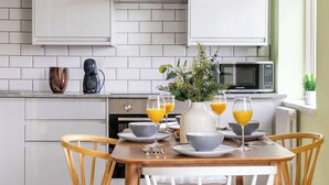 A modern kitchen with white cabinets, a microwave, and a dining table set with bowls, glasses, and a vase with flowers. - Cozy 1BR Near Hyde Park & Notting Hill (London)