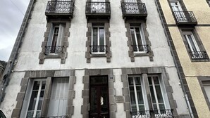 Ein mehrstöckiges Gebäude mit Stein-Fassade, mehreren Balkonen mit schmiedeeisernen Geländern und einem zentralen Eingang mit einer dunklen Tür.