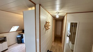 Un pasillo estrecho con suelo de madera, una pequeña cocina con lavabo y armarios, y un perchero de pared.
