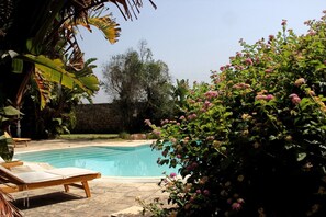 En swimmingpool med liggestole, omgivet af frodig vegetation og blomstrende planter.