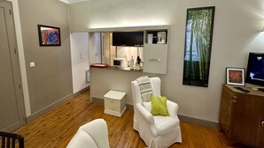 Un salon moderne avec un fauteuil blanc, une petite commode blanche, un grand miroir et un téléviseur posé sur une console en bois.