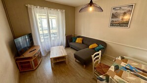 Una sala de estar con televisión, sofá, mesa y un cartel en la pared.