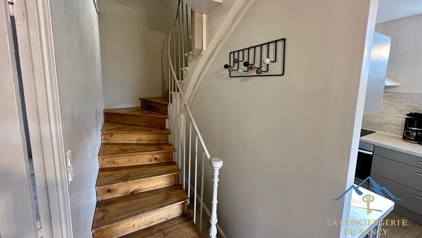 Una escalera con escalones de madera y barandillas blancas que lleva a un rellano con un perchero de pared.