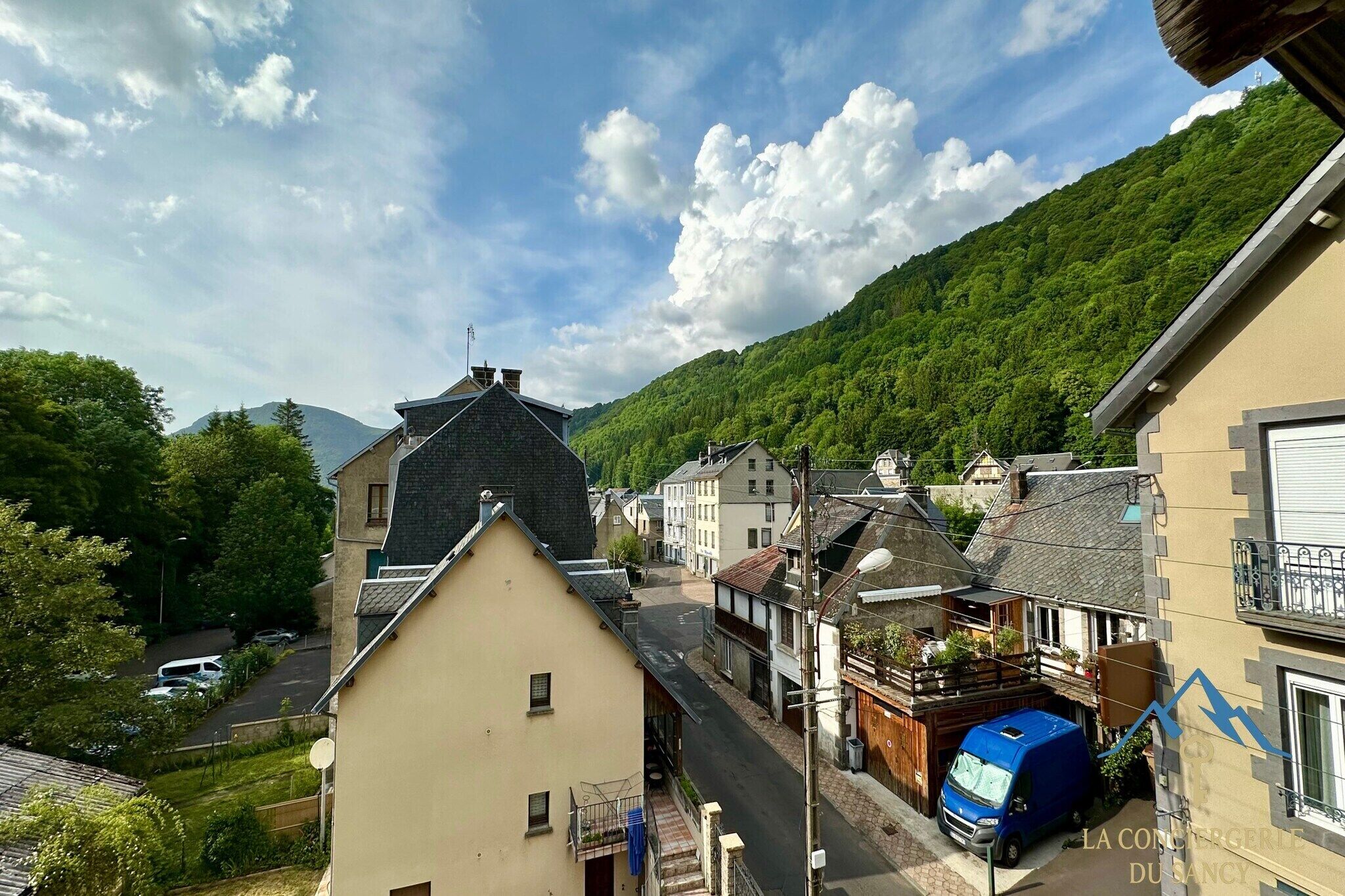 A residential street with houses, a blue van, and a mountain in the background.
