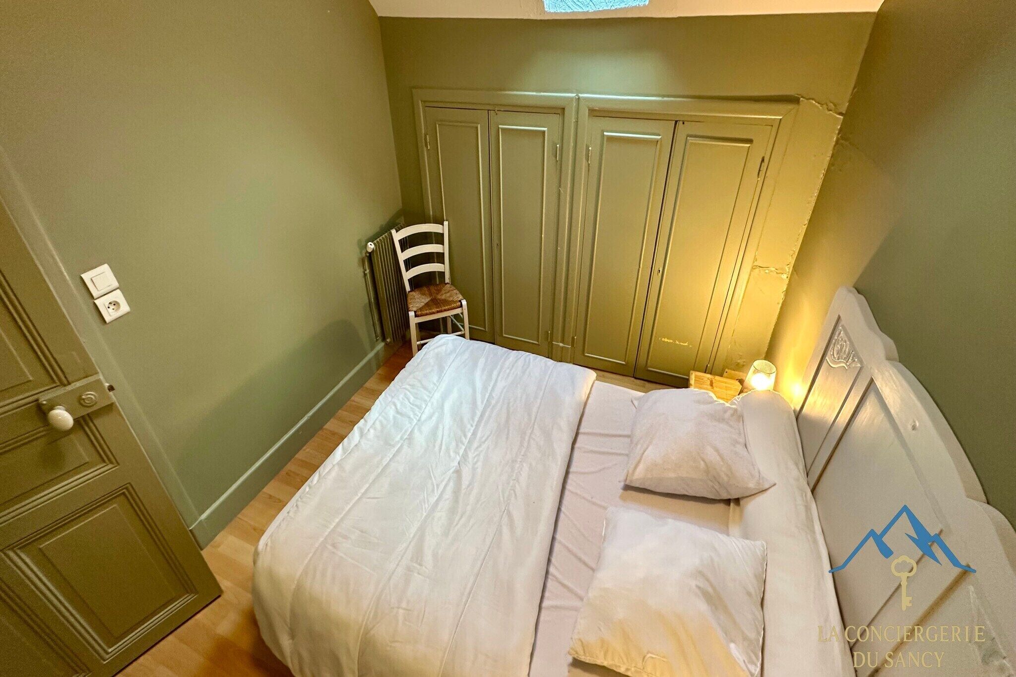 A bedroom with a bed, a chair, and a wardrobe.