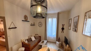 Ett mysigt vardagsrum med en soffa i trä, ett matbord med stolar, en hängande lampa och ett fönster med gardiner.