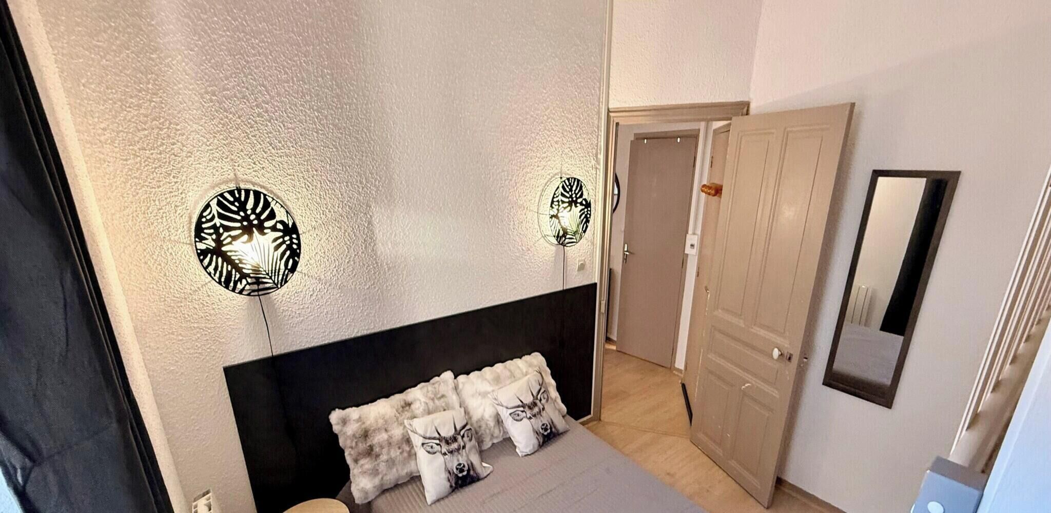 A bedroom with a bed, two wall sconces, a mirror, and a door.