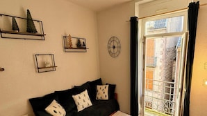Ein gemütliches Wohnzimmer mit einem dunkelgrünen Sofa, einem kleinen Holztisch und einem Fenster mit Blick auf ein Gebäude.