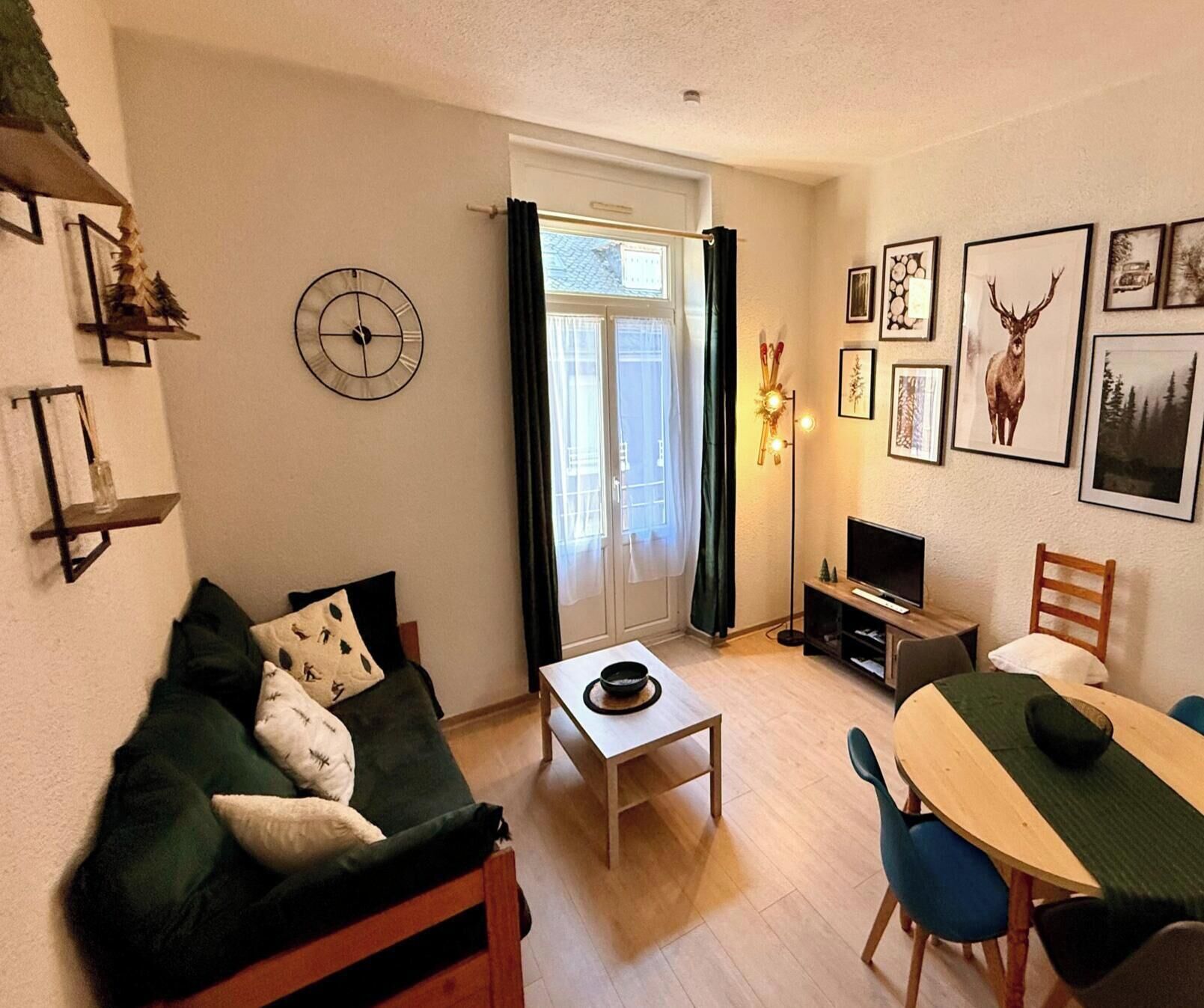 Una sala de estar acogedora con un sofá verde, una mesa de centro, un mueble para televisor y una mesa de comedor con sillas.