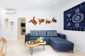 Ein modernes Wohnzimmer mit einem blauen Sofa, einem Holztisch, Wandbildern und dekorativen Wandbehängen.