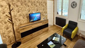 Un soggiorno moderno con un parete a motivi geometrici, una TV a schermo piatto, un tavolino da caffè in vetro con riviste, un divano nero e una poltrona gialla.