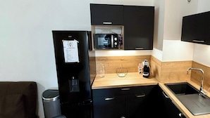 Una cucina compatta con frigorifero nero, microonde e macchina del caffè, un piano di lavoro in legno e un lavandino.