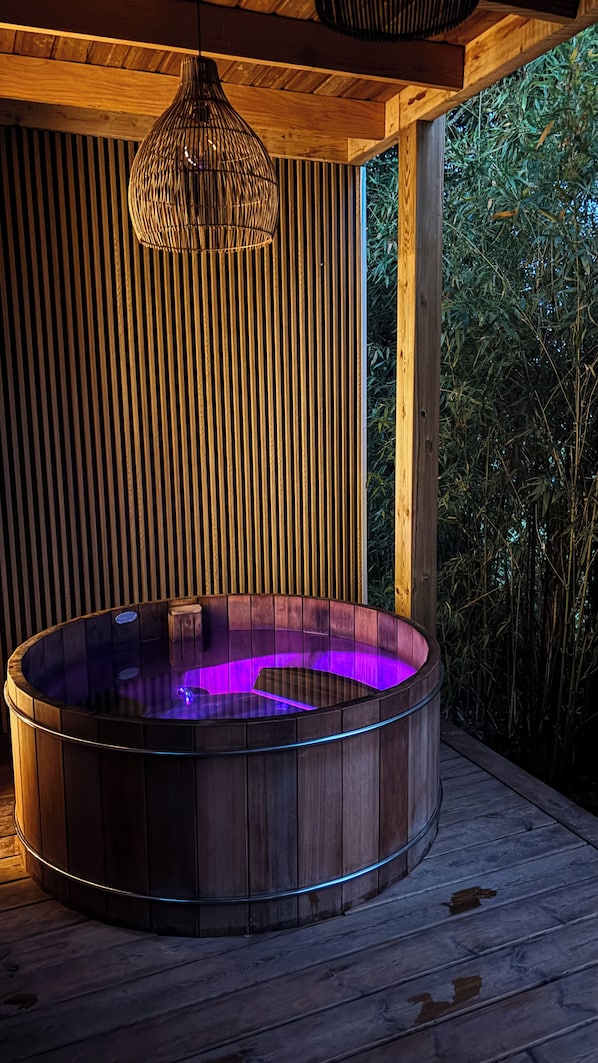 A hot tub with a wooden exterior and a glass interior, surrounded by wooden paneling and bamboo plants.