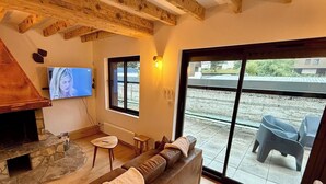 Een gezellige woonkamer met een stenen openhaard, een televisie en een groot raam met uitzicht op een patio.