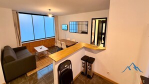 A compact living space with a sofa, a small table, a TV, and a dining area. - Modern nook by the central way (Mont-Dore)