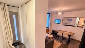 A modern living room with a dining area, a TV mounted on the wall, and a large window. - Modern nook by the central way (Mont-Dore)