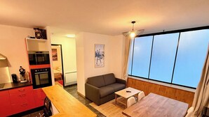 A compact living space with a kitchenette, a sofa, a small table, and a large window offering a view. - Modern nook by the central way (Mont-Dore)