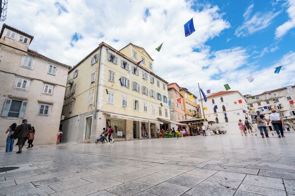Une place publique bordée de bâtiments historiques, avec une fontaine et des drapeaux.