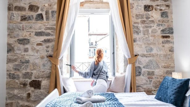 Une pièce avec un mur en pierre, un lit avec une literie blanche et une fenêtre avec des rideaux.