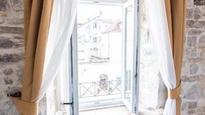Une pièce avec un mur en pierre, un banc blanc agrémenté de coussins et une fenêtre ornée de rideaux beiges.