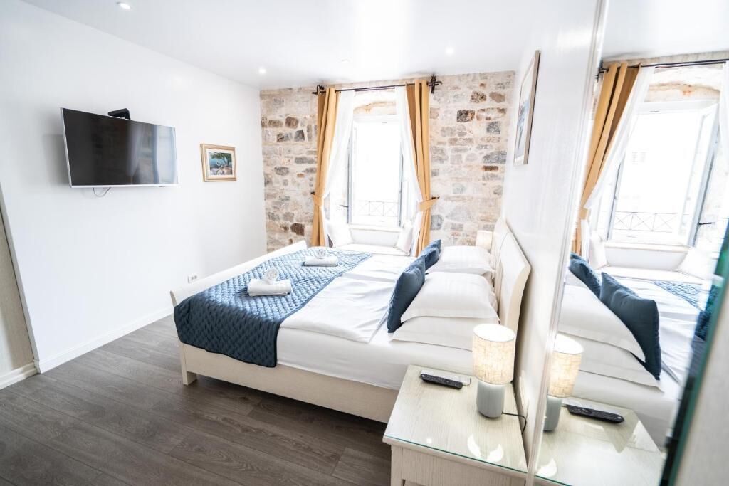 A modern bedroom with a stone wall, a bed with a blue quilt, a bedside table with a lamp, and a TV mounted on the wall.