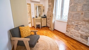 Une pièce chaleureuse avec un plancher en bois, un canapé gris agrémenté d’un coussin jaune, un tapis rond, un bureau en bois, un miroir et un mur en pierre.