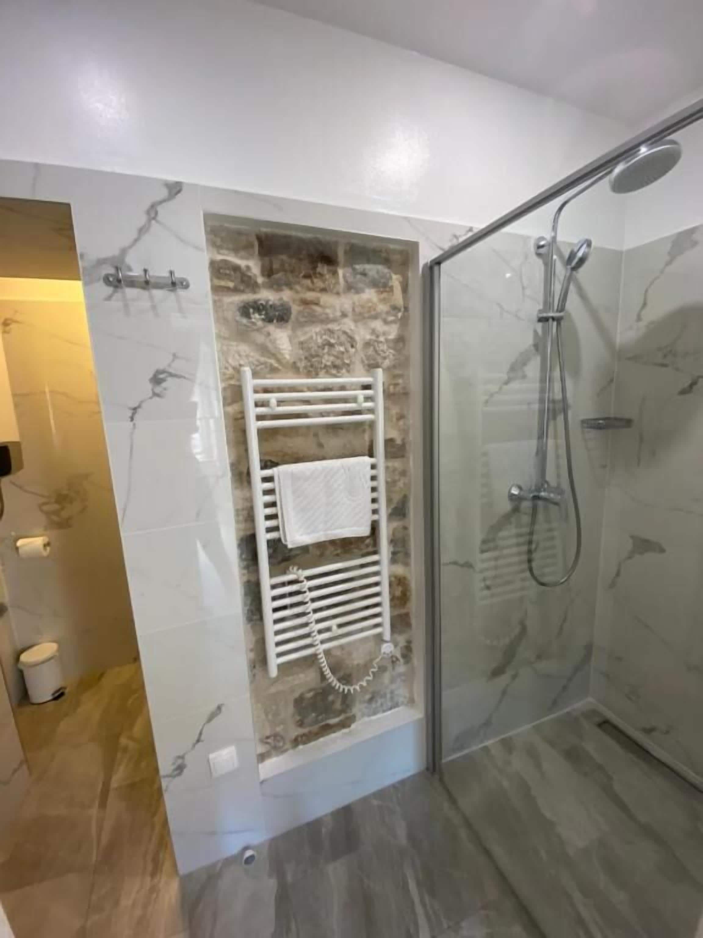 A bathroom with a glass-enclosed shower, a white towel rack, and a stone wall.