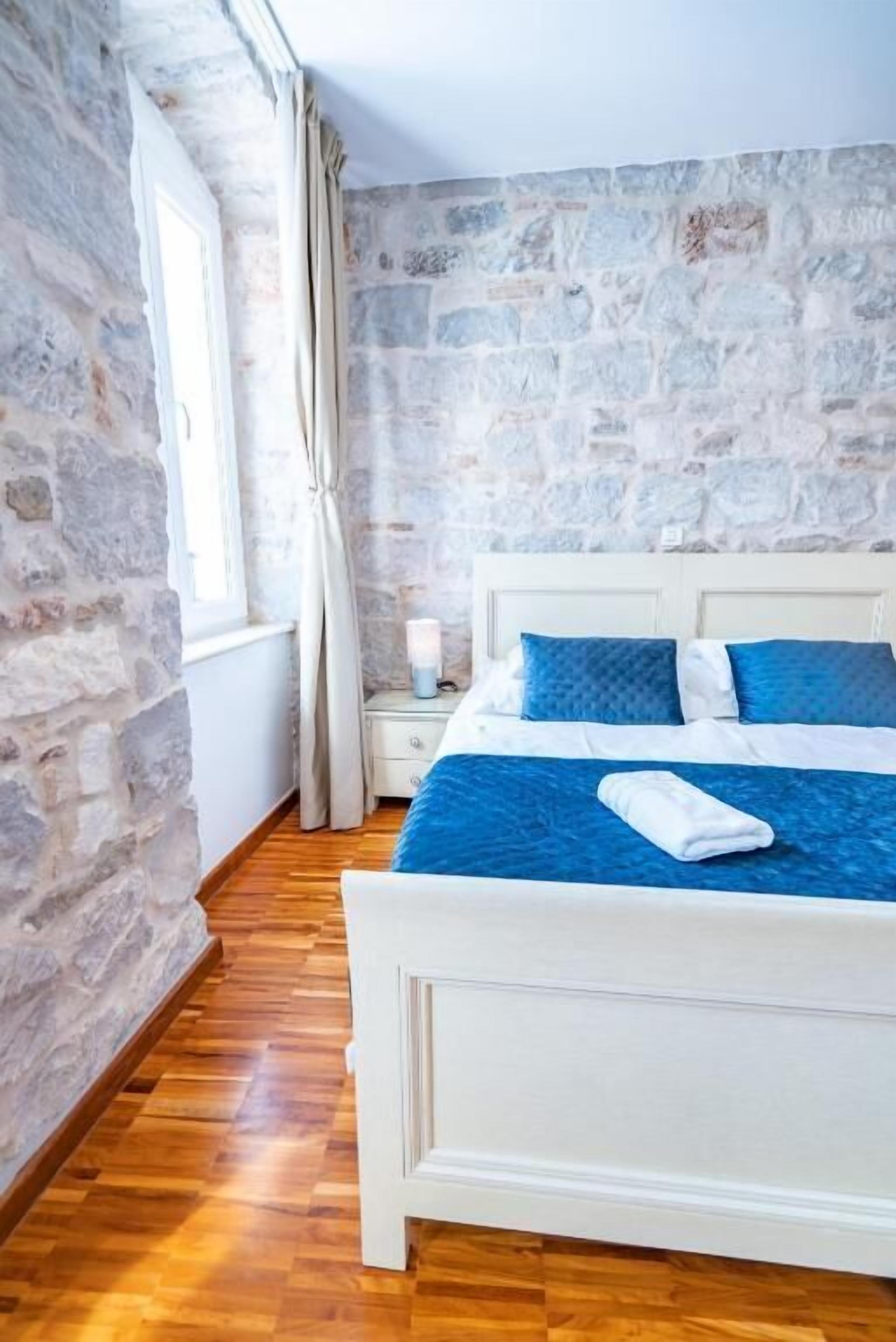 A bedroom with a stone wall, wooden floor, white bed, and blue bedding.