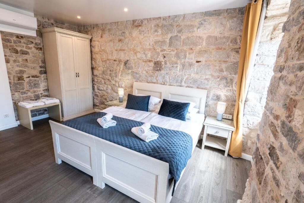 Une chambre avec un mur en pierre, un lit blanc avec une literie bleue, deux tables de chevet et une armoire.