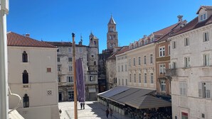 Une vaste place publique, dominée par un imposant beffroi, et bordée de bâtiments historiques à l’architecture traditionnelle.
