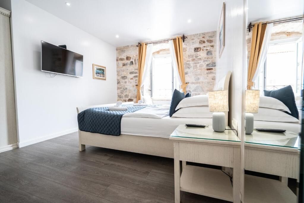 Un dormitorio con cama, mesita de noche, lámpara, televisor y pared de piedra.