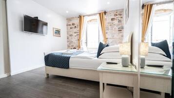 Un dormitorio con cama, mesita de noche, lámpara, televisor y pared de piedra.
