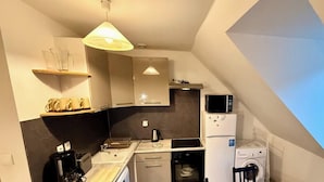 Ett kompakt kök med mikrovågsugn, kylskåp och tvättmaskin. Det finns ett litet handfat och en kaffebryggare.