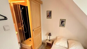 Un dormitori amb un armari de fusta, un llit amb dos almoines, dues làmpades de nit i dues imatges amb marc a la paret.