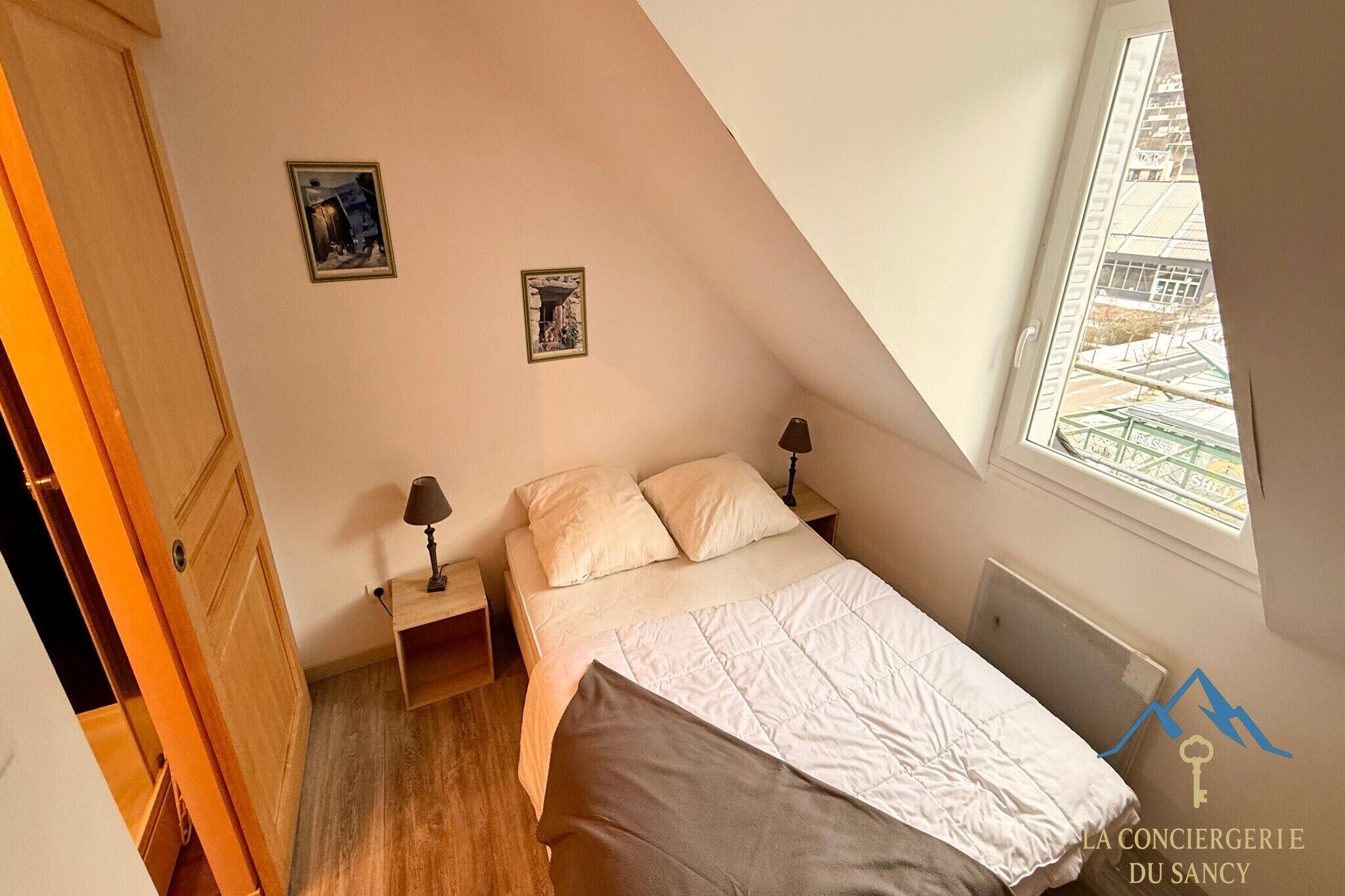 Une chambre à coucher avec un lit, deux tables de chevet, une fenêtre donnant sur un paysage agréable et une porte.