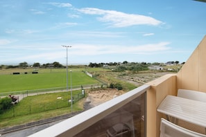 Un balcón con vistas a un campo deportivo, un coche y un edificio al fondo.